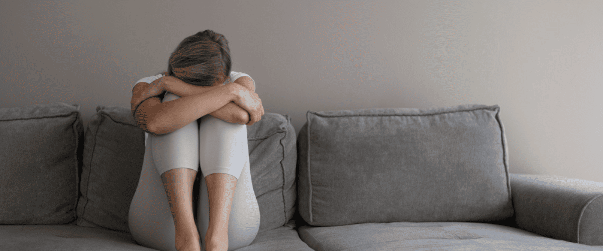 depression-girl-hugging-herself-on-sofa
